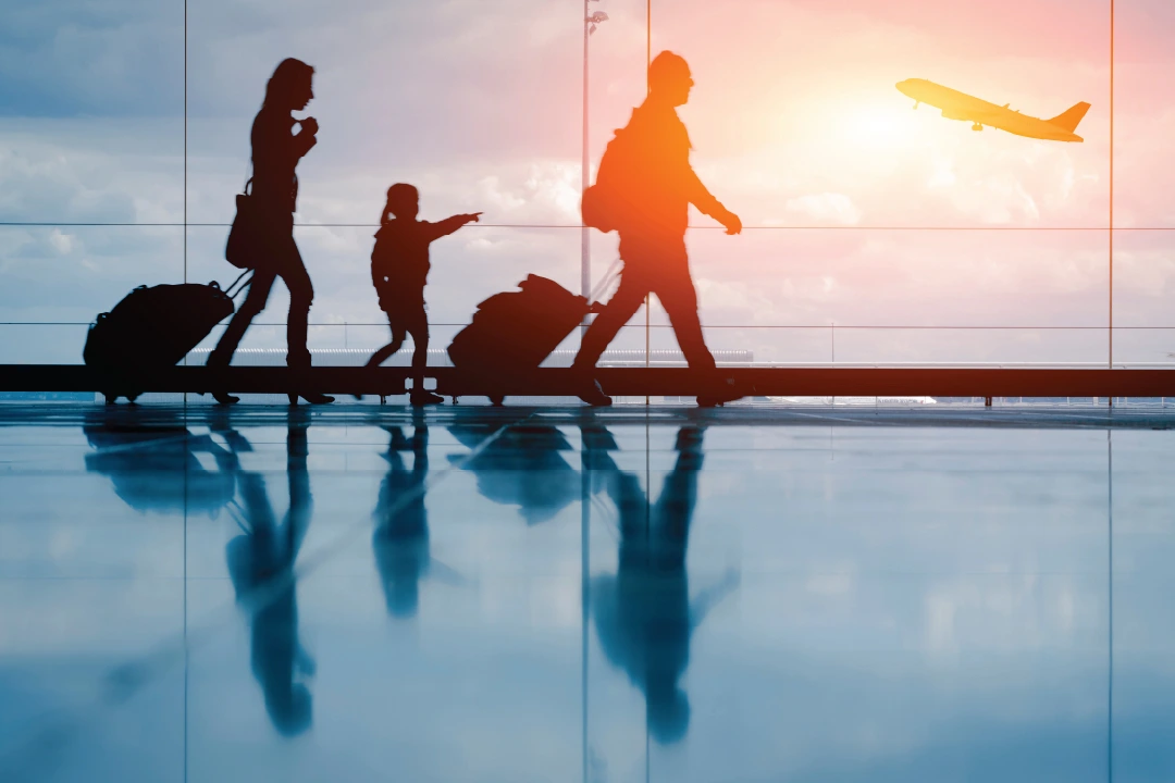 family with luggage walking through airport with jet taking off in the background